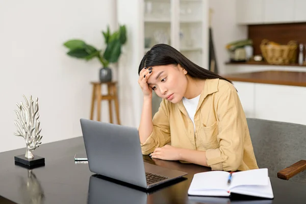 Triste mulher asiática olhando irritado e estressado, sentado na mesa, usando um laptop, pensando, sentindo-se cansado e entediado — Fotografia de Stock