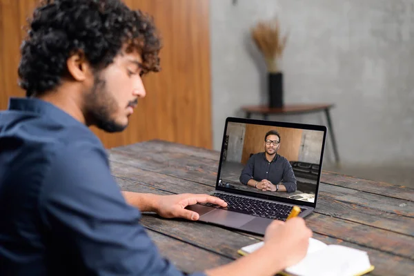 Male student studies online. Young man is watching online classes and writing a syllabus in notebook. Concept of distance study, online learning, webinars