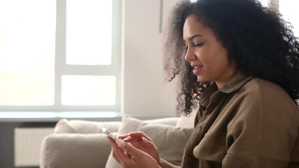 Mujer rizada joven biracial satisfecha sosteniendo el teléfono inteligente, disfrute utilizando la nueva aplicación móvil — Vídeos de Stock