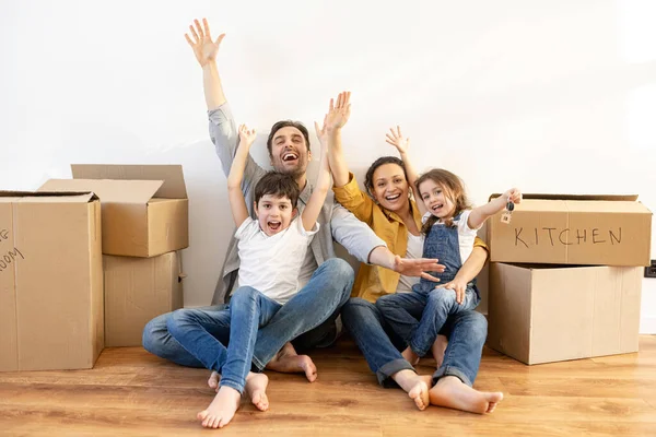 Overjoyed multiracial family of four sitting on floor surrounded cardboard boxes — Stock Photo, Image