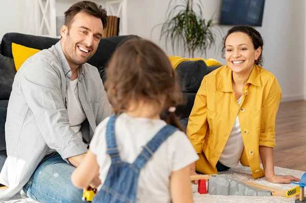 Two parents looking at the little toddler daughter playing on the floor sitting back to camera — Stock Photo, Image