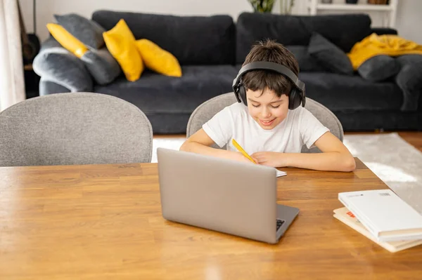 Concepto de educación online. Colegial enfocado haciendo deberes y escuchando música — Foto de Stock