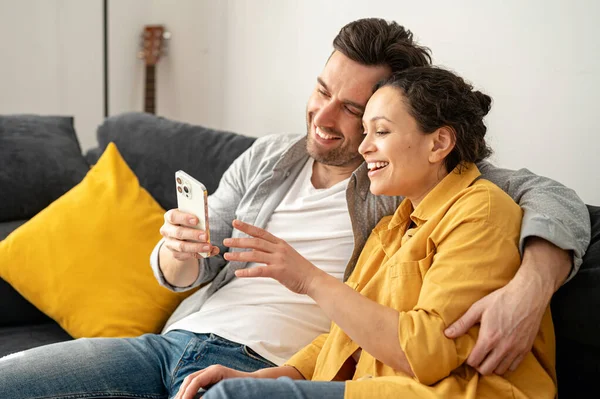 Coppia multirazziale di mezza età trascorre il tempo libero insieme a casa, utilizzando lo smartphone — Foto Stock