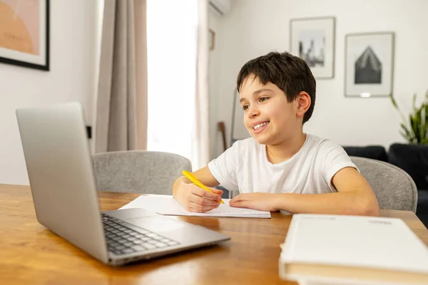 Escolar sonriente estudiando a la distancia de casa, usando una computadora portátil de moda — Foto de Stock