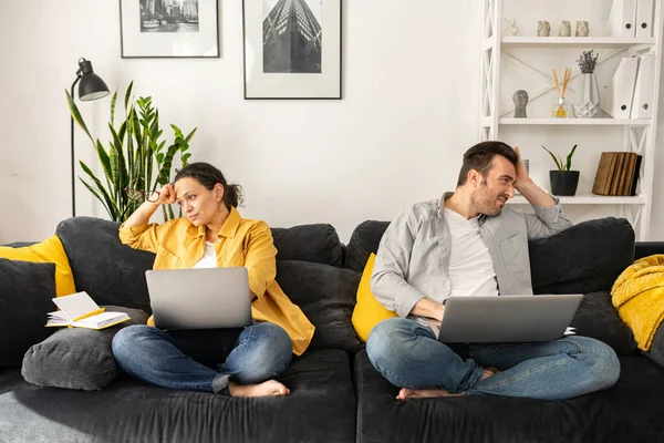 Cansado de trabalhar na distância casal de meia-idade sentado separado no sofá com laptops — Fotografia de Stock