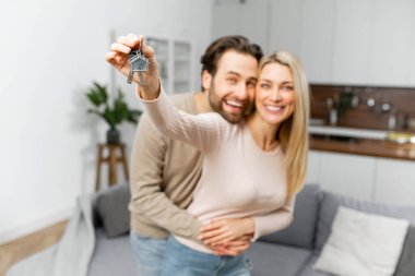 Genç beyaz evli ev sahipleri gülümsüyor, yeni bir dairenin anahtarlarını gösteriyor, kameraya bakıyor ve sarılıyor, mutfakta duruyor ve yeni bir eve taşınmayı kutluyorlar.