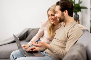 Mutlu kız arkadaş ve erkek arkadaşı kanepede oturup film izlerken dizüstü bilgisayara bakıyorlar. Kafkasyalı çift boş vakitlerini geçiriyorlar.