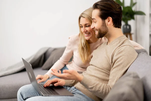 Feliz namorada e seu namorado olhando para a tela do laptop enquanto se senta no sofá, assistindo filmes. Casal caucasiano apaixonado passar o tempo de lazer — Fotografia de Stock