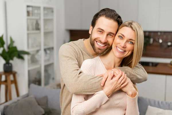 Relaciones armónicas. Feliz pareja casada posando para una foto en la cocina. El marido caucásico abrazando a su esposa por detrás. Los corazones más felices hacen los hogares más felices —  Fotos de Stock