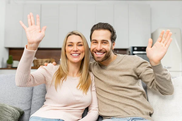 Schermo video con allegra coppia caucasica che guarda la fotocamera e saluta. Webcam vista di donna sorridente e il suo uomo seduto sul divano e saluto — Foto Stock