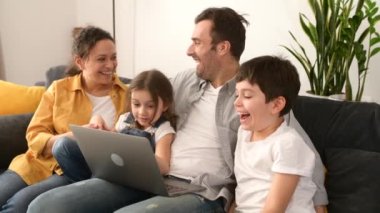 Dört kişilik mutlu bir aile rahat bir dairede kanepede dizüstü bilgisayar kullanıyor.