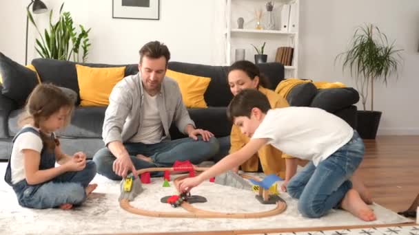 Любимая семья из четырех человек проводит выходные вместе дома, родители и двое детей играют в игрушки — стоковое видео