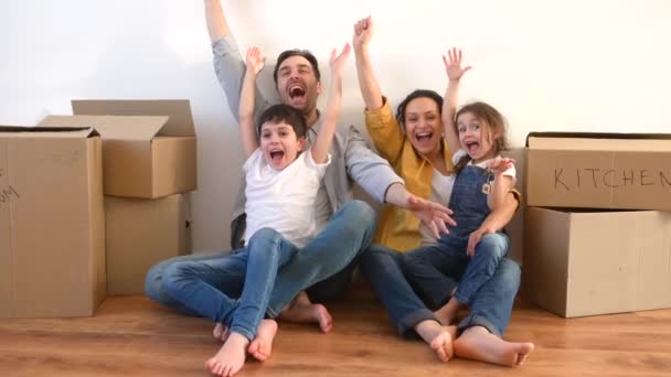 Överlycklig multiracial familj med fyra sittande på golvet omgivna kartonger — Stockvideo