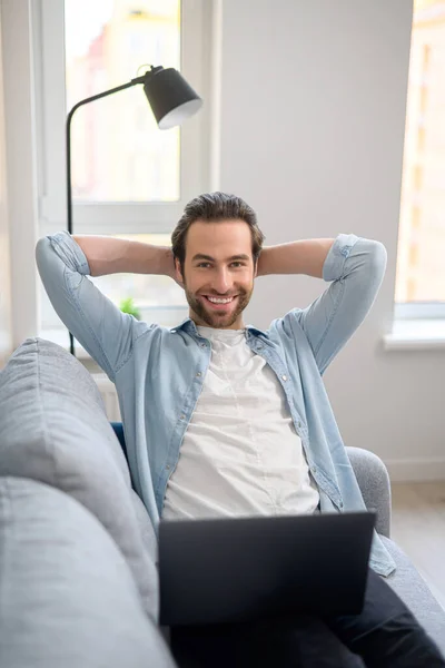 Lavoro a distanza. Colpo verticale per l'uomo caucasico che riposa sul divano mentre lavora sul computer portatile a casa — Foto Stock