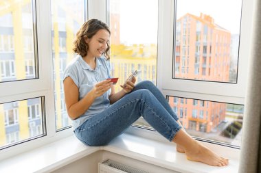 Elinde cep telefonu olan, gülümseyen Kafkas ergen bir kız, çevrimiçi işlem yapmak için kredi kartı numarasını giriyor. Yemek sipariş eden, online alışveriş yapan bir kadın.