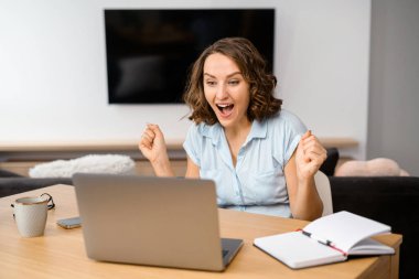 Gol başarısı. Neşeli, neşeli genç kadın evet diye bağırıyor ve zafer jesti olarak ellerini kaldırıyor. Merkez ofisteki dizüstü bilgisayarın önünde oturuyor.