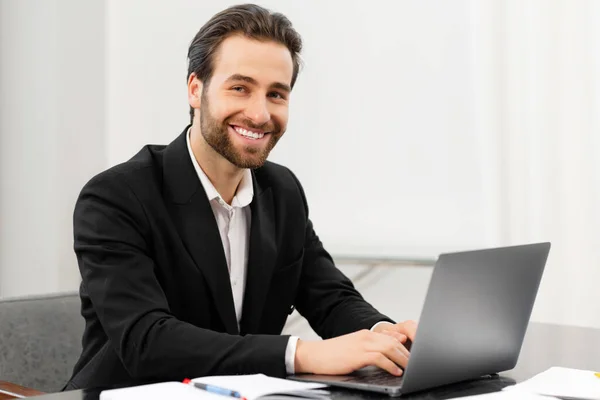 Šťastně se usmívající obchodník pracující z úřadu. Úspěšný muž sedící za stolem, s notebookem, vyvinul projekt — Stock fotografie