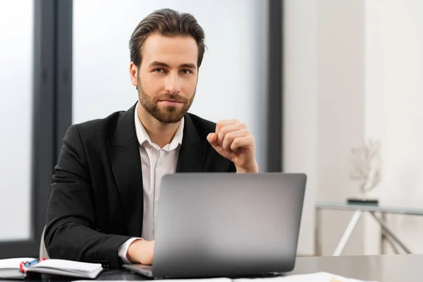 Glad manlig entreprenör tittar på kameran. Glada kaukasiska mannen bär formella kläder sitter vid bordet och använder laptop på kontoret — Stockfoto