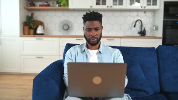 使用笔记本电脑坐在沙发上的沮丧的非裔美国人 — 图库视频影像