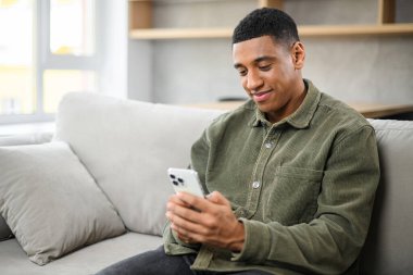 Yakışıklı adam mesajlaşmak, mesajlaşmak için akıllı telefon kullanıyor. Akıllı ve rahat giyinen genç bir adam elinde telefonla oturmuş, bir mesaj yazıyor.