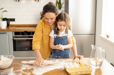 Orta yaşlı anne ve küçük tatlı kız birlikte yemek pişiriyorlar.