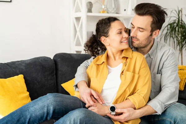 Gentile e bella coppia innamorata seduta in abbraccio sul comodo divano di casa — Foto Stock