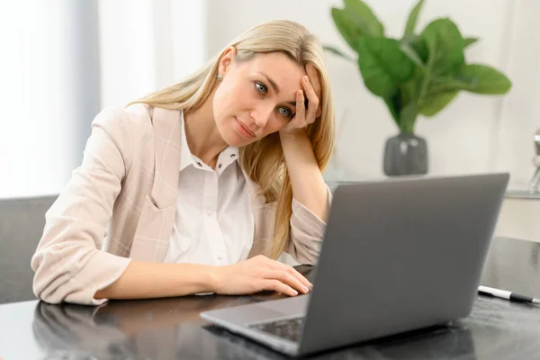 Funcionária de escritório entediada sentada na mesa em frente ao laptop no escritório, olhando para o lado e sentindo-se triste. Jovem pensativa não tem inspiração para o trabalho — Fotografia de Stock