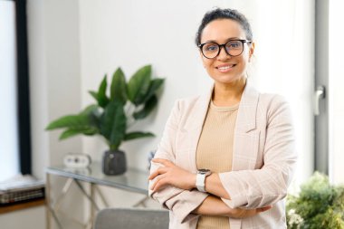 Çağdaş ofiste kolları çapraz duran neşeli kadın girişimci.