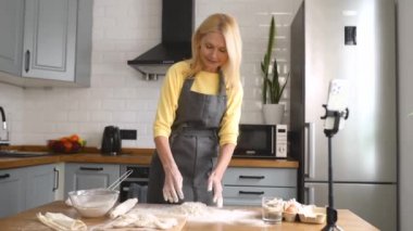 Önlüklü, orta yaşlı bir kadın hamur hazırlıyor ve sosyal medyada yayınlıyor.