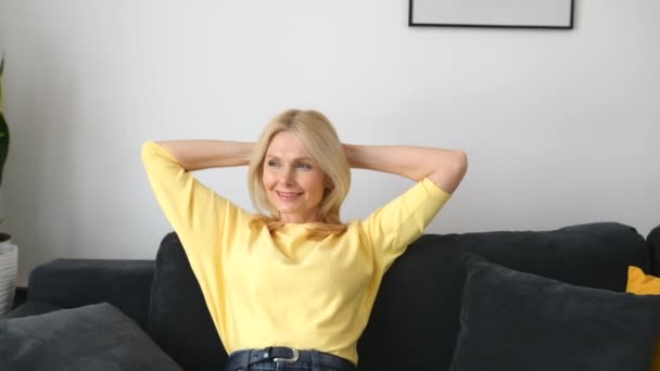 Беззаботная женщина средних лет с длинными волосами, сидящая на диване — стоковое видео
