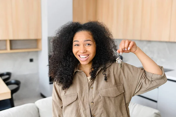 Счастливая молодая женщина держит ключи с брелком в виде домика. Улыбающаяся брюнетка владеет ключами от новой недвижимости, счастливый покупатель собственного имущества — стоковое фото
