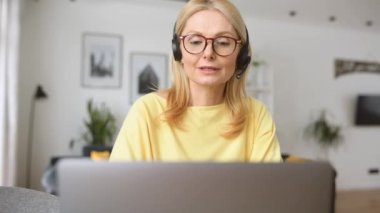 Orta yaşlı, kulaklık takan bir kadın uzaktan konuşuyor.