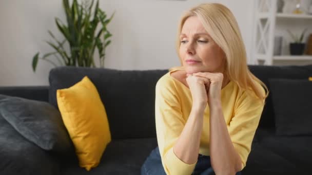 Zdenerwowana starsza pani w żółtym swetrze siedząca na kanapie — Wideo stockowe