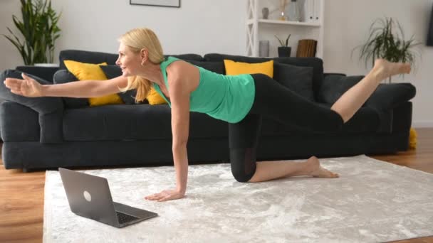 Orta yaşlı kadın aktif bir yaşam sürüyor, evde egzersiz yapıyor, internetten yoga öğreniyor. — Stok video