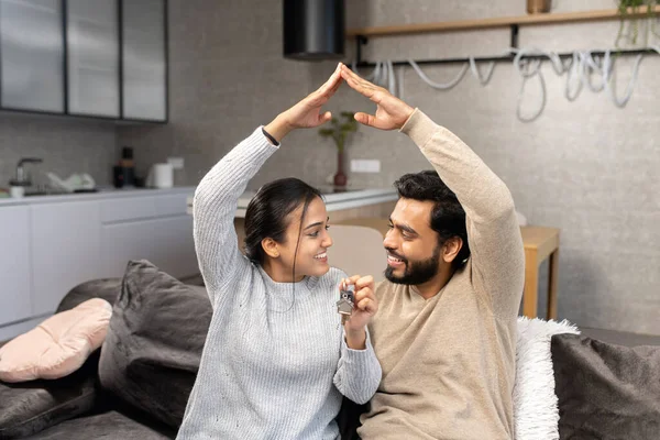 Щаслива індійська подружня пара, яка показує нові ключі від будинку до камери, виставляючи в приміщенні. Власний дім, нерухомість і житло. — стокове фото
