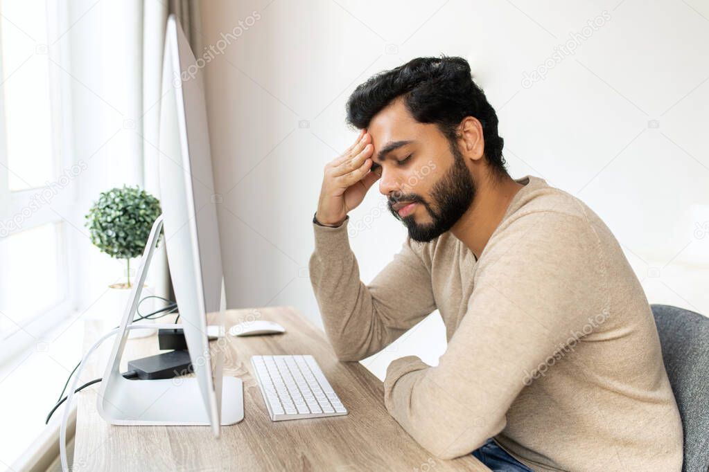 Tired mixed-race hindu male entrepreneur feel eye strain from online work with laptop, indian man sits at the table and massaging eyes, feels headache