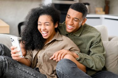 Aşırı mutlu çift kanepede dinleniyor ve ellerinde akıllı telefonlar, online piyango kazananını kutlarken, bahis zafer anı, inanılmaz bir fırsat ya da davetiye, internet satışı