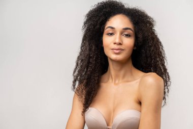 Çekici, çekici, esmer, kıvırcık saçlı ve kameraya bakan kadının yatay görüntüsü.