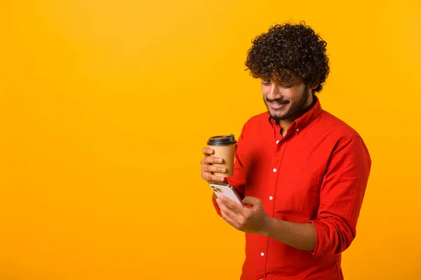 Уверенный в себе ближневосточный мужчина в смарт-рубашке, смс-ках на смартфоне и с бумажной чашкой кофе на вынос — стоковое фото