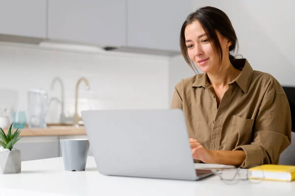 Femme freelance rêvant avec une tasse de café du matin, femme souriante assise à la table avec ordinateur portable, regarde l'écran, attendant l'inspiration — Photo