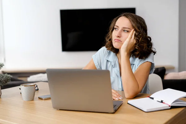 Mulher branca jovem olhando irritado e estressado, sentado na mesa, usando um laptop, pensando e olhando para longe, sentindo-se cansado e entediado — Fotografia de Stock