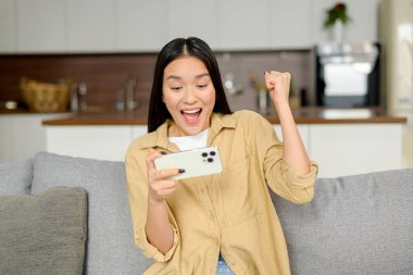 Asyalı genç bir kadının evde akıllı telefon kullanmasına ve kanepede oturmasına şaşırdım. Şaşırmış mutlu bayan mesaj okuyor ve seviniyor.