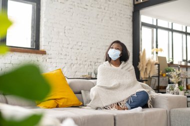 Onaylanmış viral hastalığı olan, üzgün, üzgün, karantina ve kendini izole etme süresince evdeki kanepede oturan çok kültürlü bir kadın.