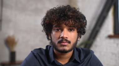 Ofis masasında oturup kameraya bakan mutlu Hintli adamın portresi.