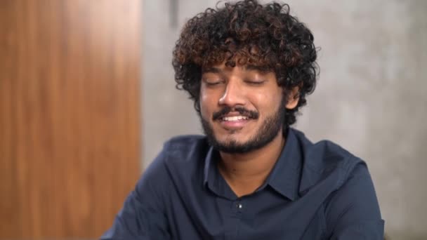 Видеопортрет уверенного умного индийского работника, сидящего за столом в современном офисе — стоковое видео
