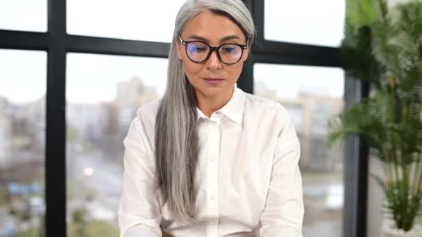 Empresária madura ativa ocupada em óculos sentados à mesa na frente do laptop — Vídeo de Stock