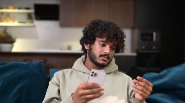 Sırıtkan Hintli adamın elinde banka kartı ve akıllı telefon var.