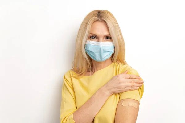 Portrait of caucasian senior woman wearing medical mask showing her arm with band aid after coronavirus Covid-19 vaccine — Fotografia de Stock