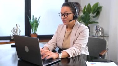 Gülümseyen kadın çağrı merkezi çalışanı çevrimiçi iletişim için kulaklık ve laptop kullanıyor.