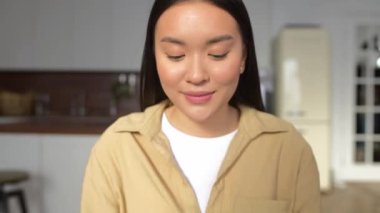 Zeki Asyalı kadın kameraya bakıyor, dizüstü bilgisayarın önünde oturuyor.